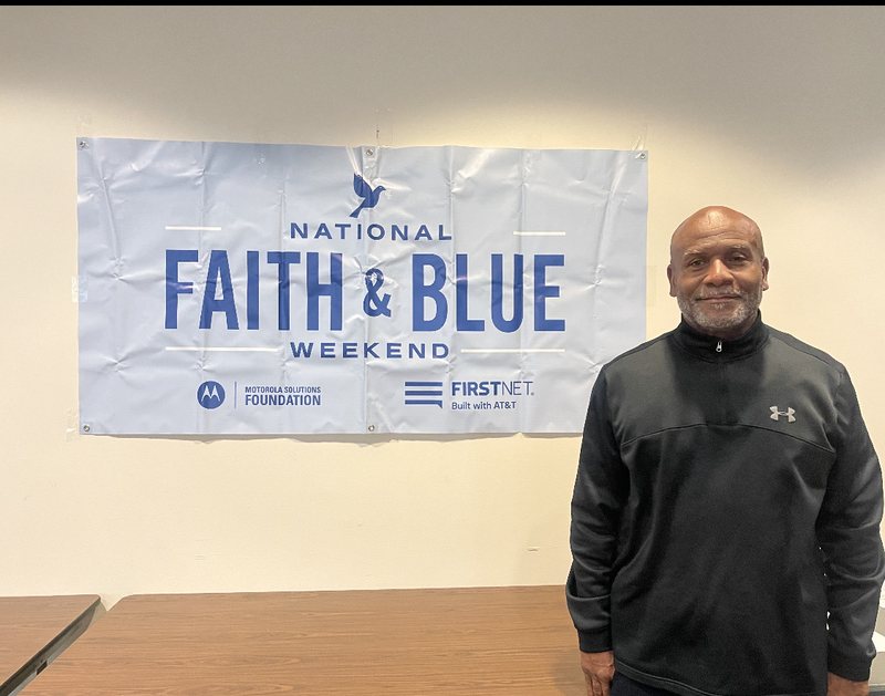 Moses Robinson beside the National Faith and Blue Weekend banner